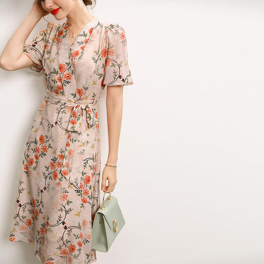 Woman in a pink floral embroidered mulberry silk midi dress with short sleeves, holding a mint green handbag.