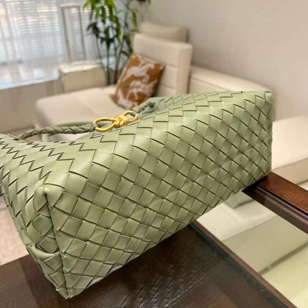 Sage green woven leather handbag with gold hardware on a glass table, modern living room background