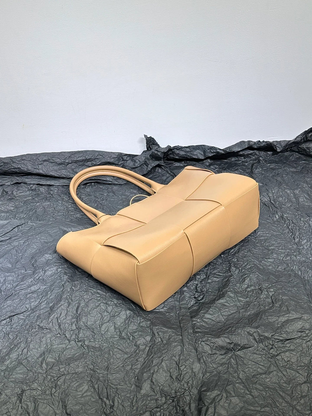 Beige woven leather tote bag with double handles on a textured dark background