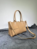 Beige leather woven handbag with double handles and adjustable shoulder strap on textured surface