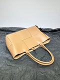 Tan woven leather tote bag with double handles on a textured black surface