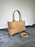 Tan woven leather tote bag with double handles and matching detachable strap on gray fabric