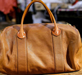 Large brown leather weekend duffle bag with dual handles on a wooden surface, ideal for travel