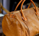Brown leather duffle bag with top handles and gold zipper, ideal for travel or gym use