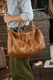 Person holding brown leather duffle bag with dual handles, travel and weekend bag style