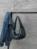 Black woven leather hobo bag and denim jacket on a metal rack against a concrete wall