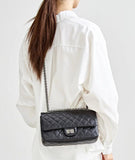 Woman in white outfit carrying a black quilted leather shoulder bag with silver chain strap