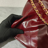 Close-up of quilted burgundy leather shoulder bag with gold chain strap, held by gloved hand.