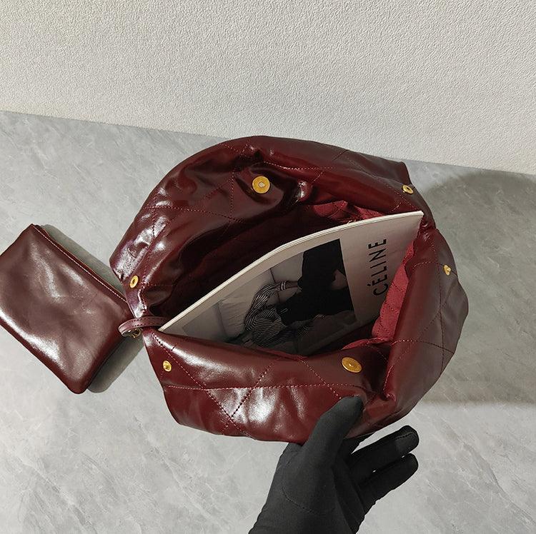 Large burgundy quilted leather shoulder bag with gold snap buttons, open to show spacious interior and matching pouch, minimalist designer handbag on marble surface.