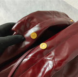 Close-up of burgundy quilted leather shoulder bag with gold magnetic snap closure.