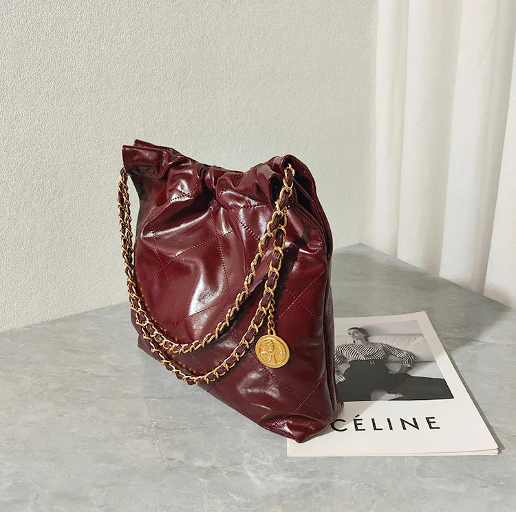 Burgundy quilted leather shoulder bag with gold chain strap on marble surface