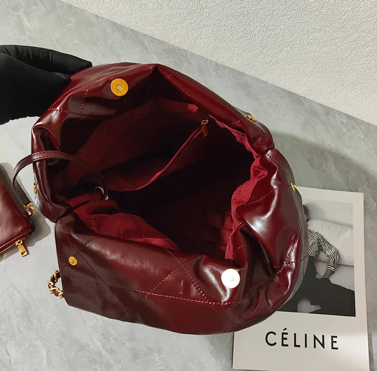 Large burgundy quilted leather shoulder bag with gold hardware, open to show spacious interior, placed on a marble surface.