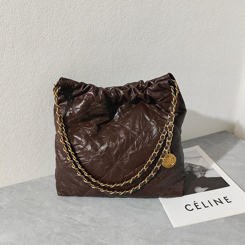 Brown quilted leather shoulder bag with gold chain strap on a table