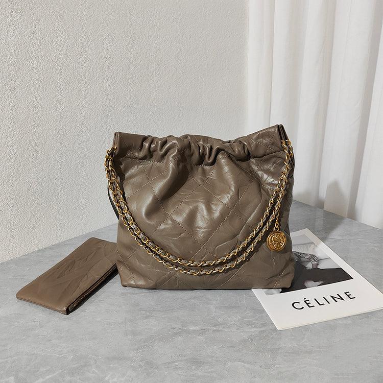 Large taupe quilted leather shoulder bag with gold chain strap and matching wallet on a marble surface