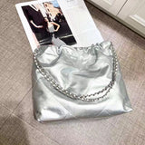 Large silver quilted leather shoulder bag with gold-tone chain strap on a textured surface.