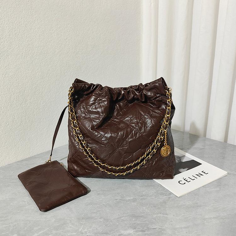 Brown leather shoulder bag with gold chain strap and matching pouch on a marble table