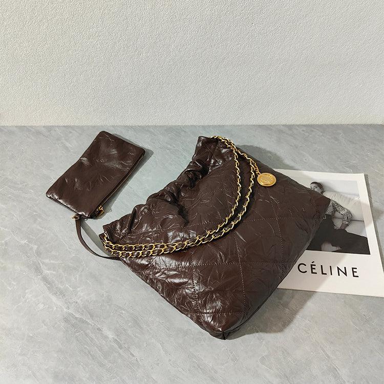 Brown quilted leather shoulder bag with gold chain strap and matching pouch on marble surface