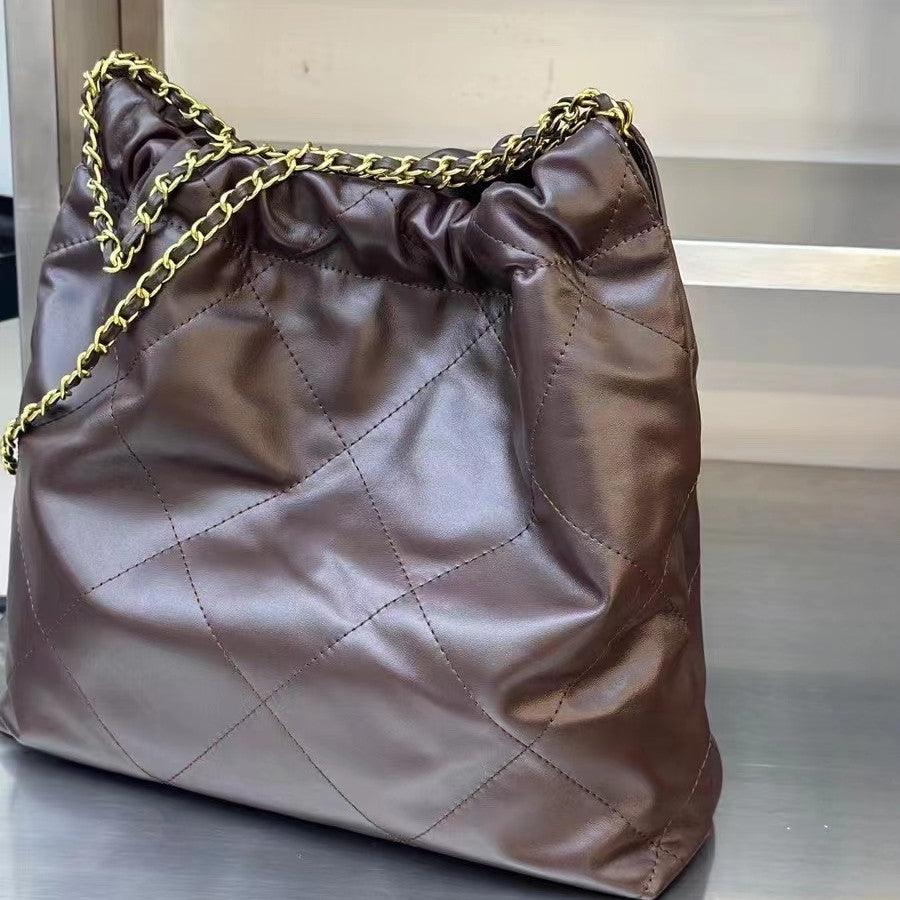 Brown quilted leather shoulder bag with gold-tone chain on a metal surface