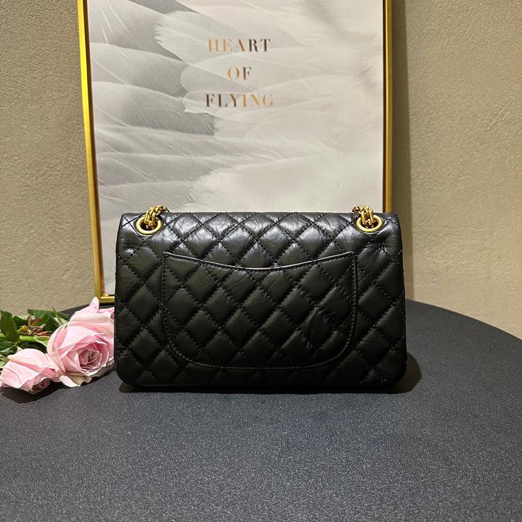 Woman in white shirt carrying black quilted leather shoulder bag with gold chain strap