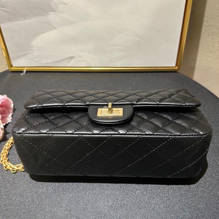 Woman in white shirt carrying black quilted leather shoulder bag with gold chain strap