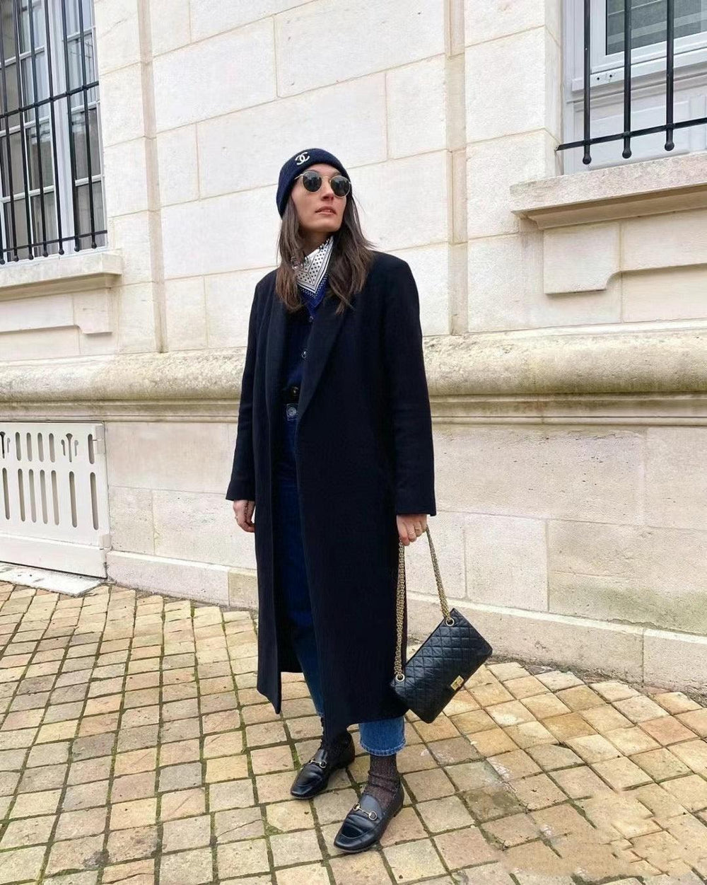 Woman in white shirt carrying black quilted leather shoulder bag with gold chain strap