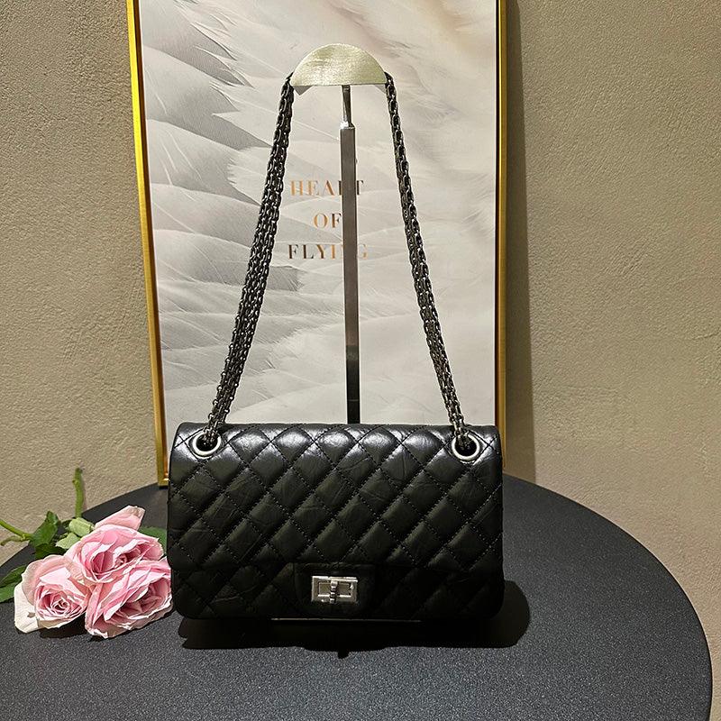 Woman in white outfit carrying a black quilted leather shoulder bag with silver chain strap