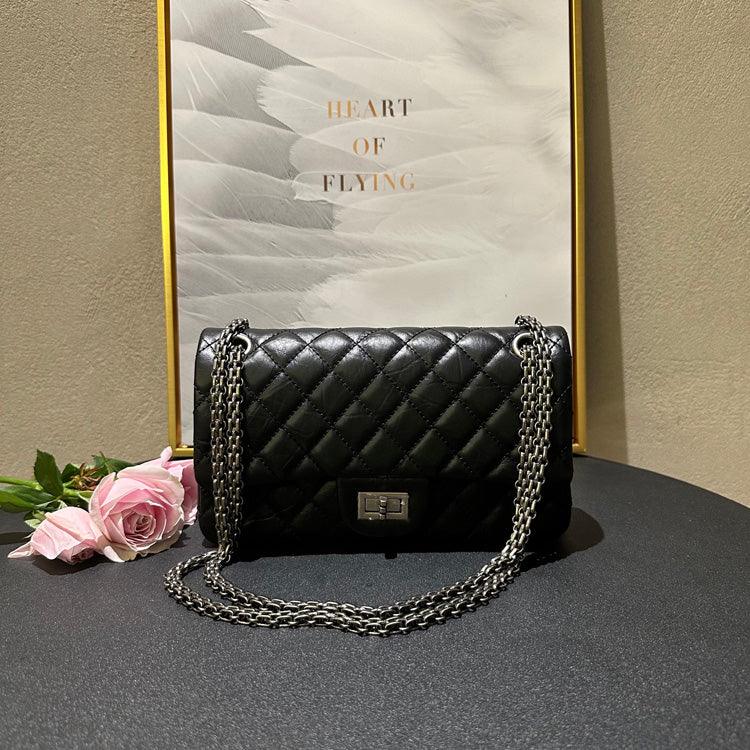 Woman in white outfit carrying a black quilted leather shoulder bag with silver chain strap