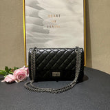 Woman in white outfit carrying a black quilted leather shoulder bag with silver chain strap