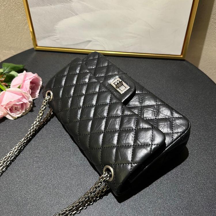 Woman in white outfit carrying a black quilted leather shoulder bag with silver chain strap