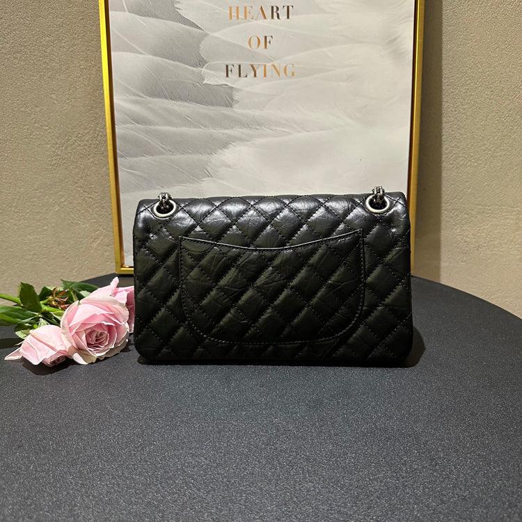 Woman in white outfit carrying a black quilted leather shoulder bag with silver chain strap