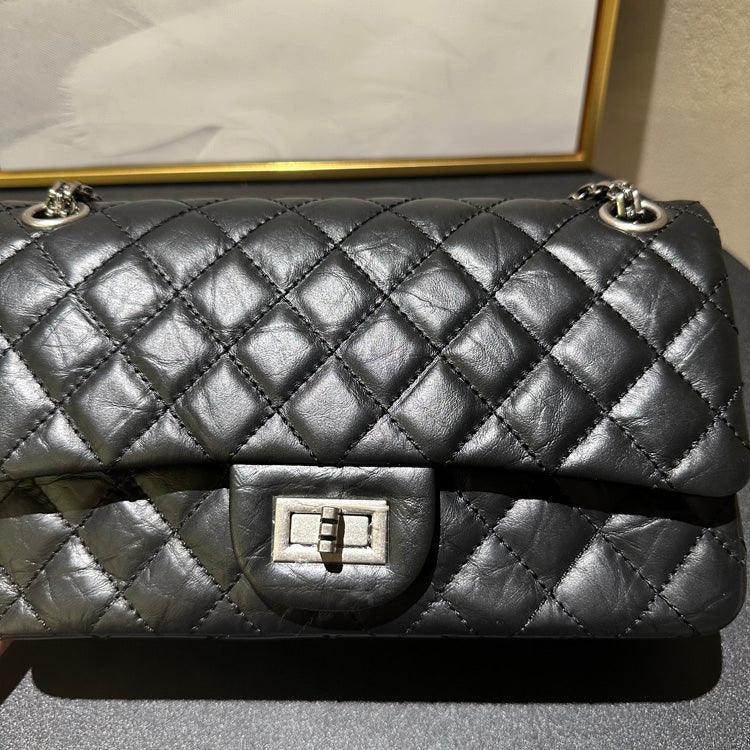 Woman in white outfit carrying a black quilted leather shoulder bag with silver chain strap