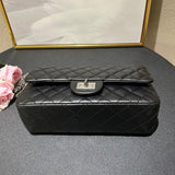 Woman in white outfit carrying a black quilted leather shoulder bag with silver chain strap