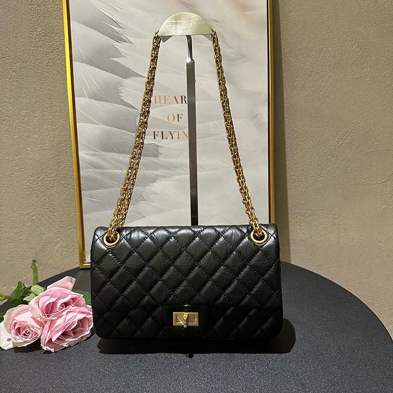 Woman in white shirt carrying black quilted leather shoulder bag with gold chain strap