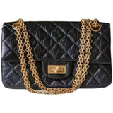 Woman in white shirt carrying black quilted leather shoulder bag with gold chain strap