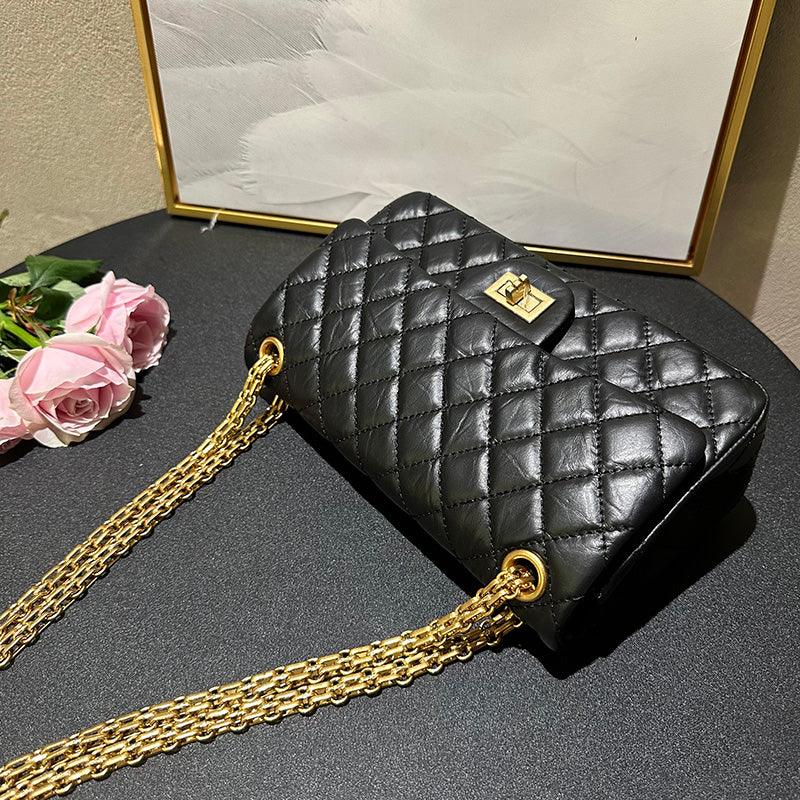 Woman in white shirt carrying black quilted leather shoulder bag with gold chain strap