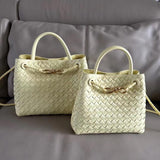 Two cream woven leather shoulder bags with top handles and gold metal buckles on a sofa