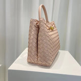 Beige woven leather shoulder bag with gold metal buckle and dual handles on display pedestal.