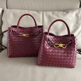 Burgundy woven leather shoulder bags with gold metal buckles on a beige sofa.