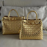 Gold woven leather shoulder bags with knotted handles and metal buckles on a sofa