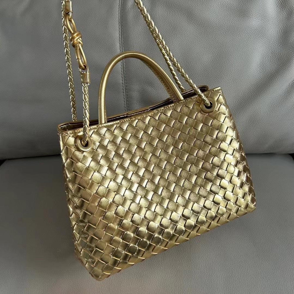 Gold woven leather shoulder bag with knotted strap and metal accents on a grey sofa