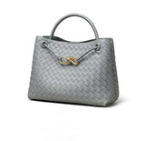 Grey woven leather shoulder bag with gold metal buckle and top handle on white background