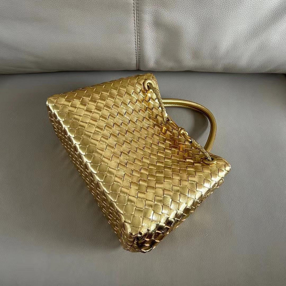 Gold woven leather shoulder bag with knotted handle and metal buckle on a couch.