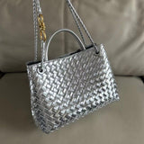 Silver woven leather shoulder bag with metal buckle detail and chain strap on beige sofa