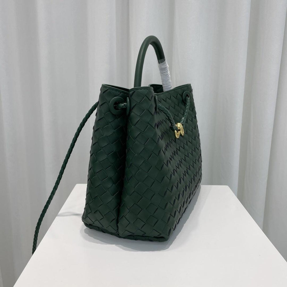 Dark green woven leather shoulder bag with braided strap and gold metal buckle on display