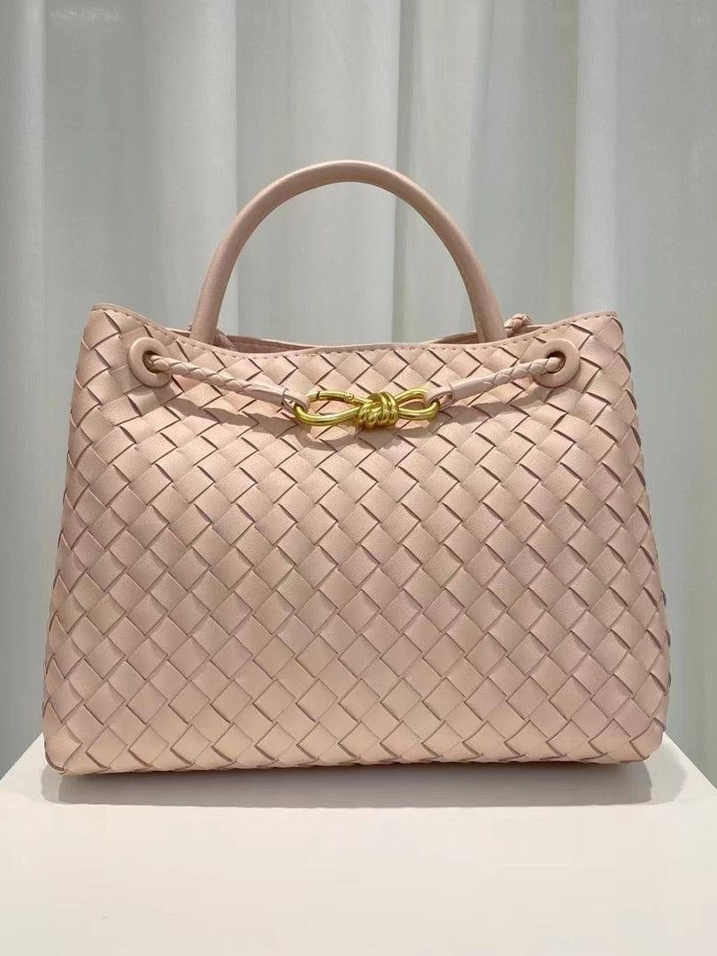 Beige cowhide leather woven shoulder bag with gold metal buckle and top handles on display