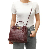 Woman wearing a burgundy woven leather shoulder bag with gold buckle and crossbody strap