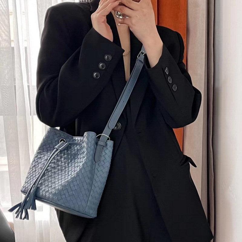 Woman wearing black blazer with medium blue woven lambskin leather bucket bag and drawstring tassel