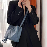 Woman wearing black blazer with medium blue woven lambskin leather bucket bag and drawstring tassel