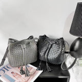 Two handwoven lambskin leather drawstring bucket bags in grey and black on a table.