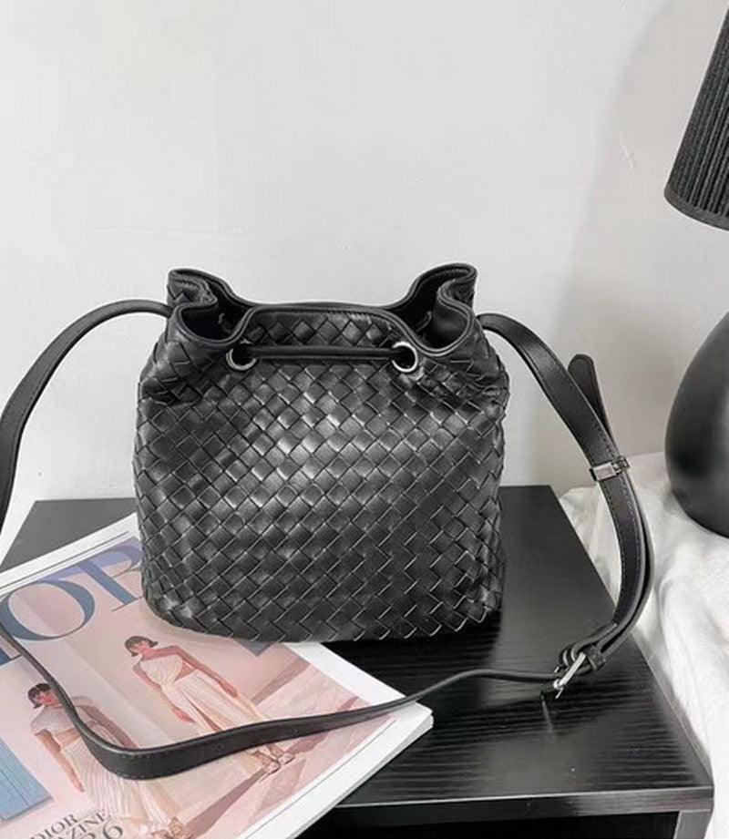 Handwoven black lambskin leather bucket bag with drawstring and shoulder strap on table